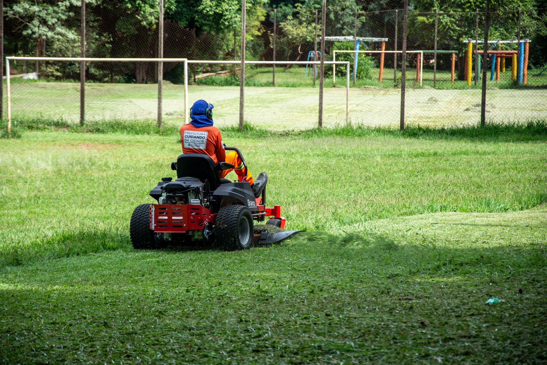 Person mowing grass on a ride-on mower in a fenced park field
