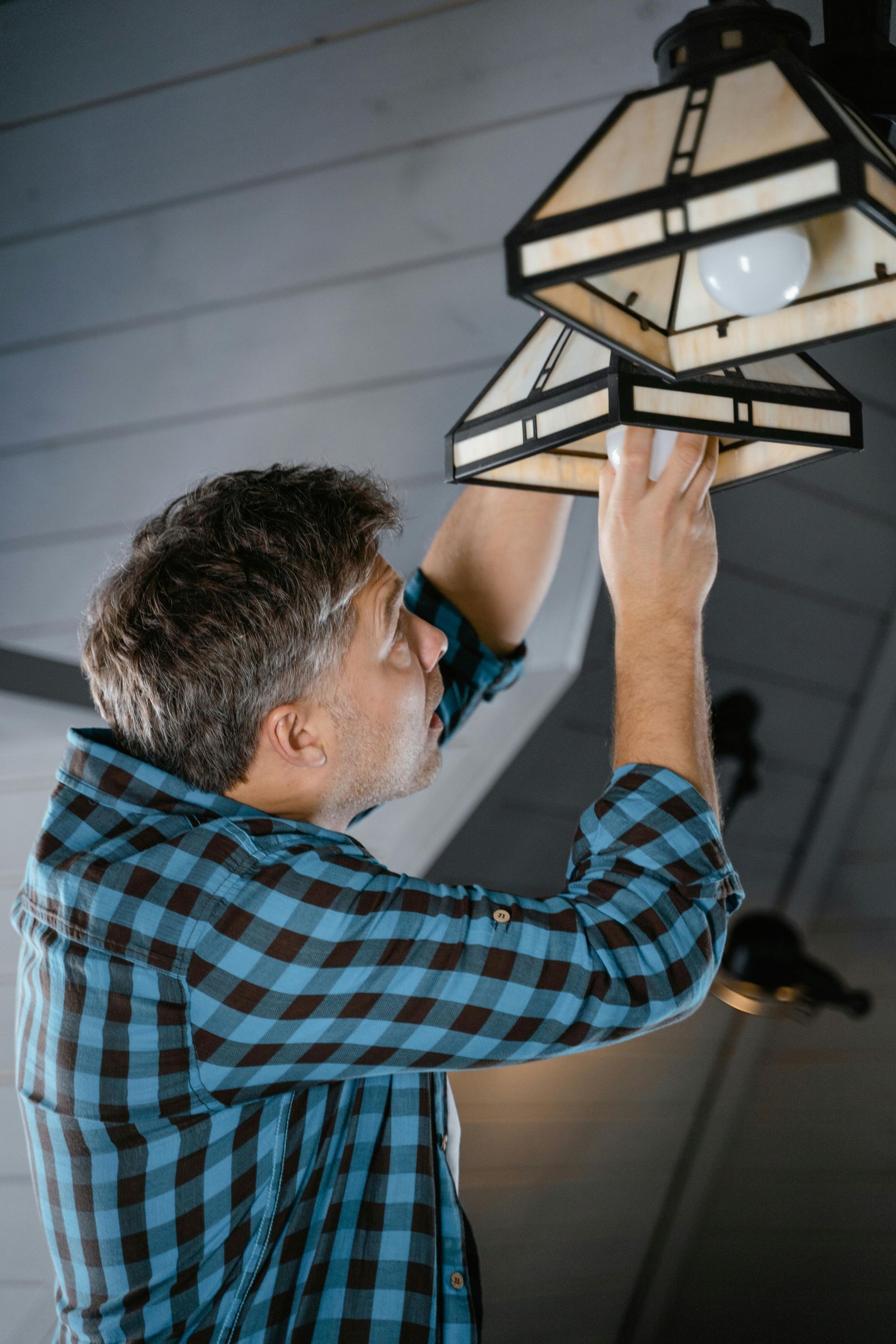 Man in blue plaid shirt adjusting ceiling light fixtures indoors