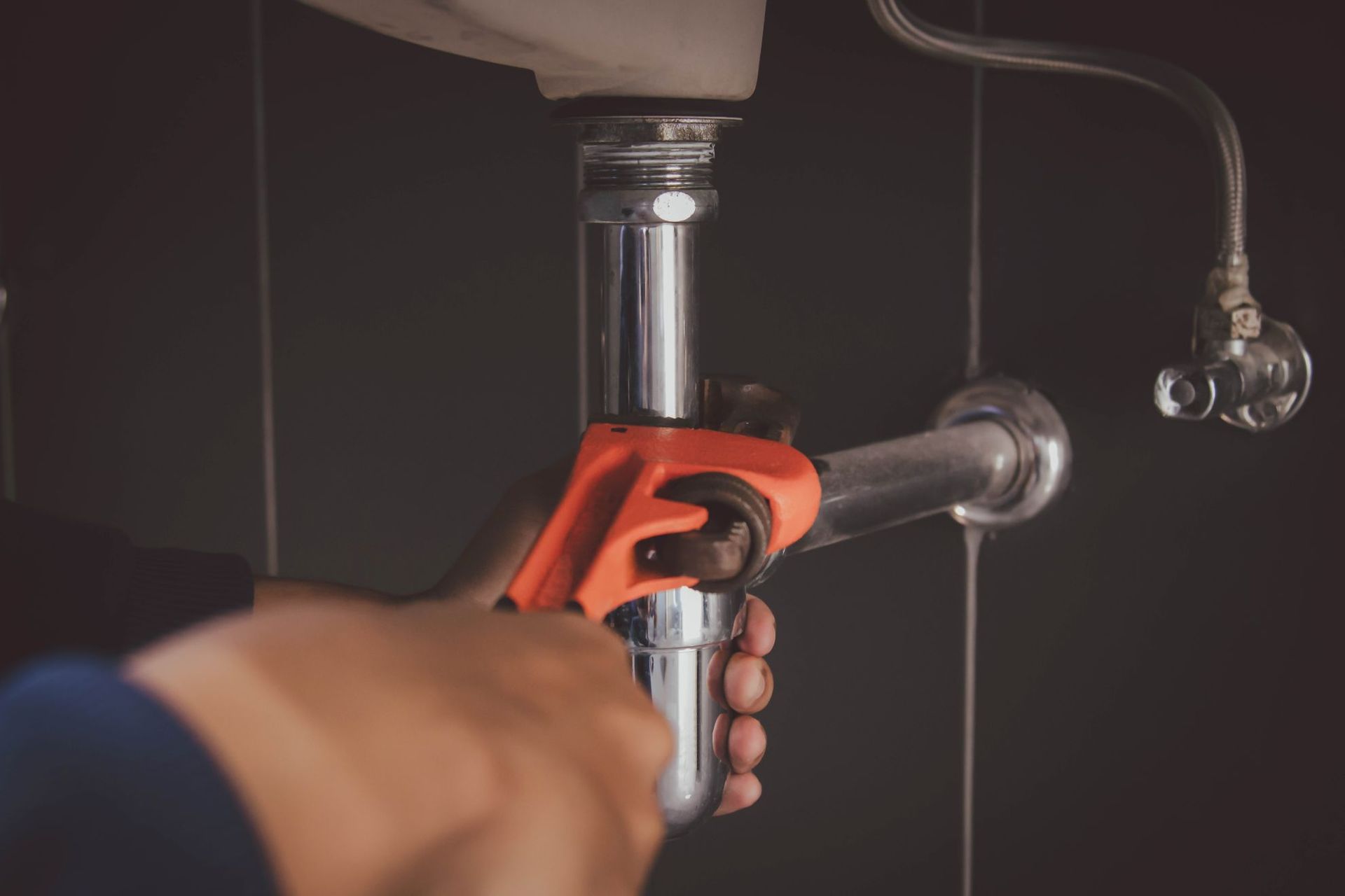 Hands using a red pipe wrench to tighten a silver faucet under a sink