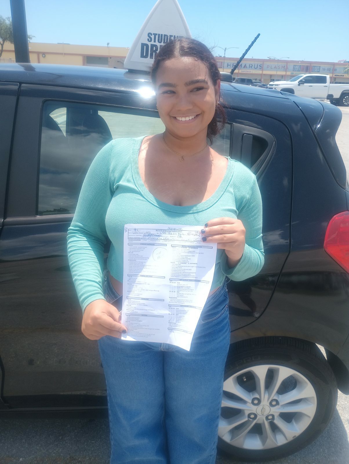 A woman is holding a driving license in front of a car