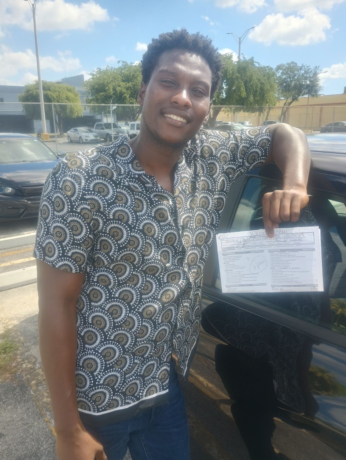 A man is standing next to a car holding a driving license