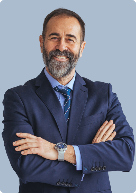 A professional with a beard, wearing a navy suit and patterned tie, stands with arms crossed against a light blue background.