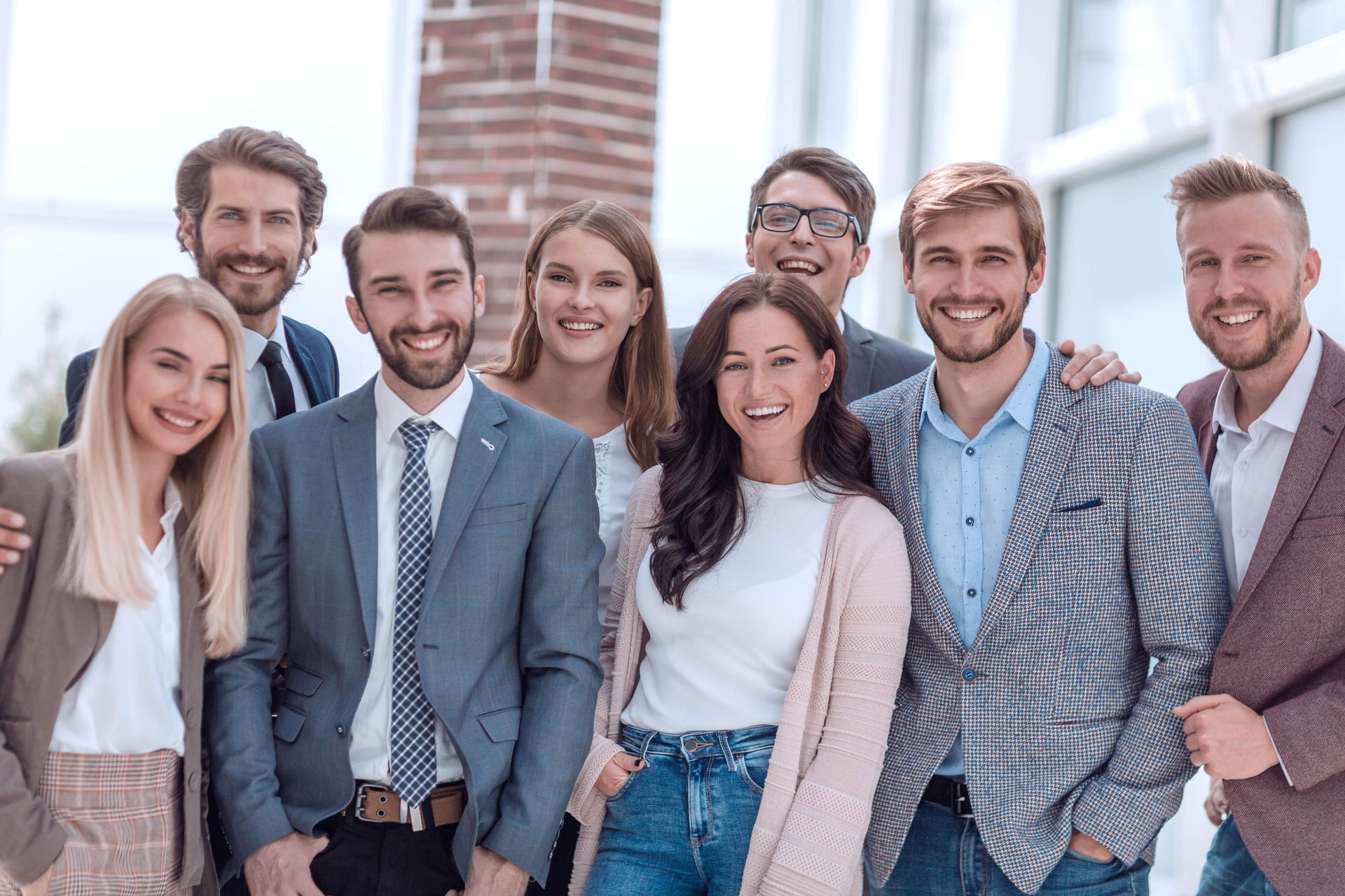 A group of diverse professionals in business attire smiling together in a bright, modern office space.