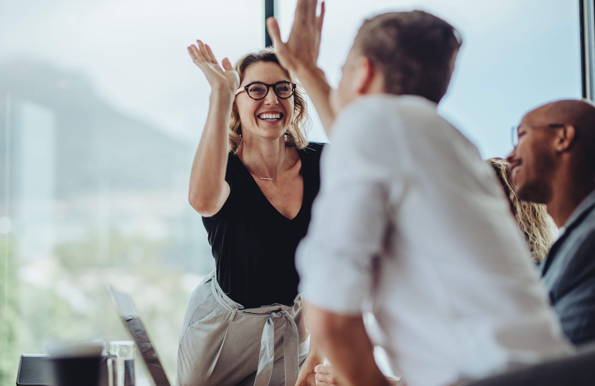 A woman in a black shirt high-fives a colleague in a bright office, with another person smiling nearby.