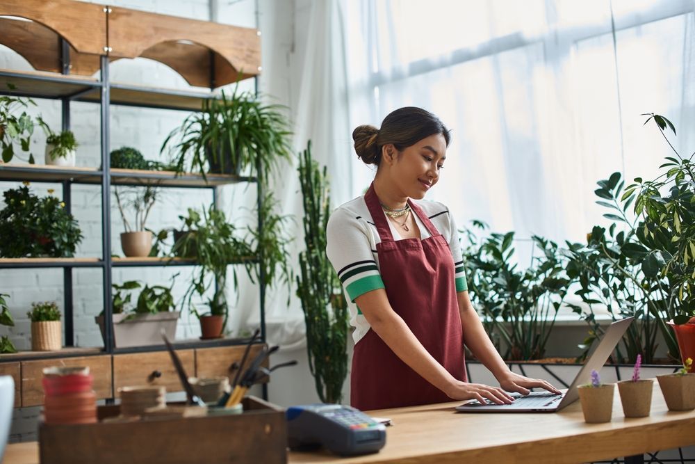 A woman is standing at a counter using a laptop computer.