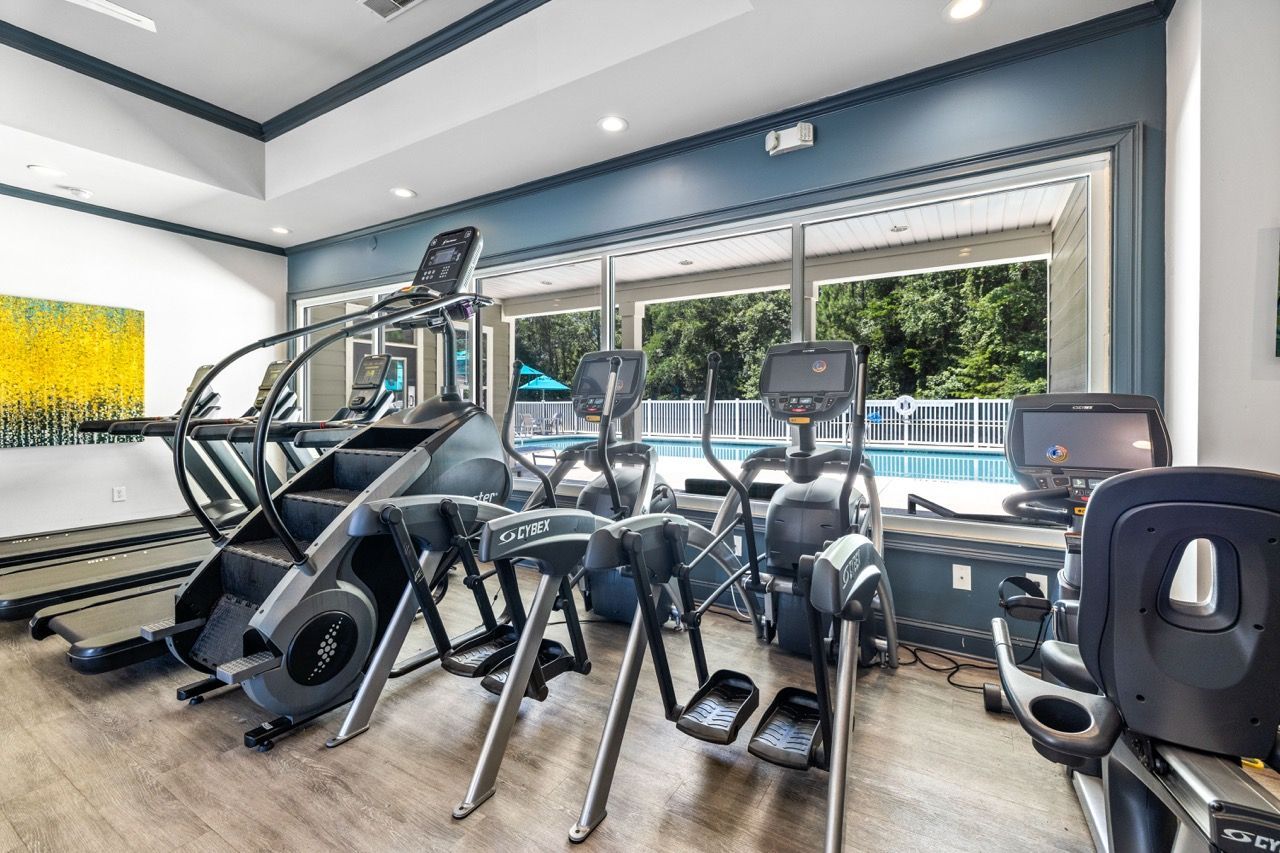 Gym with treadmills and ellipticals facing large windows overlooking a pool.