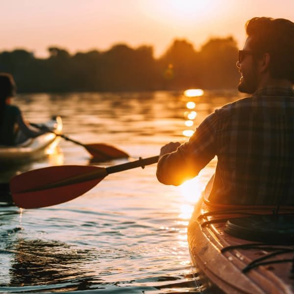 Two people kayaking on a calm lake during a warm, golden sunset.