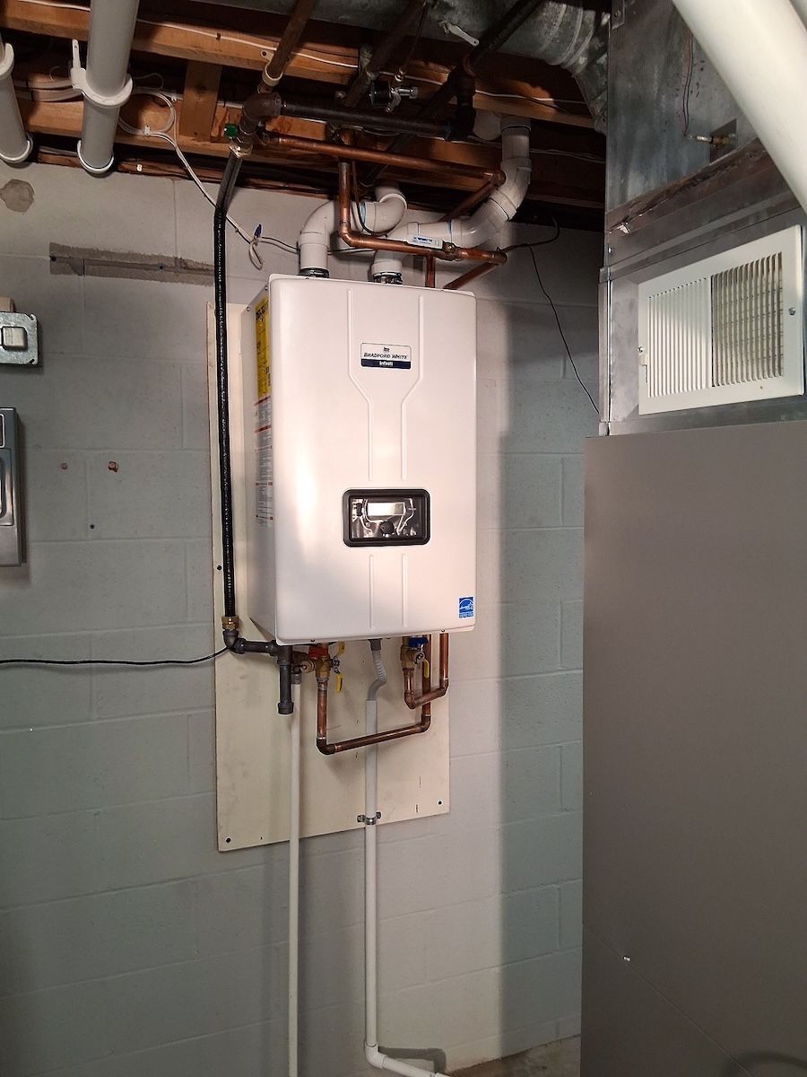 Woman in a black patterned dress looks at phone as barefoot girl in pink dress twirls in a sunny room.