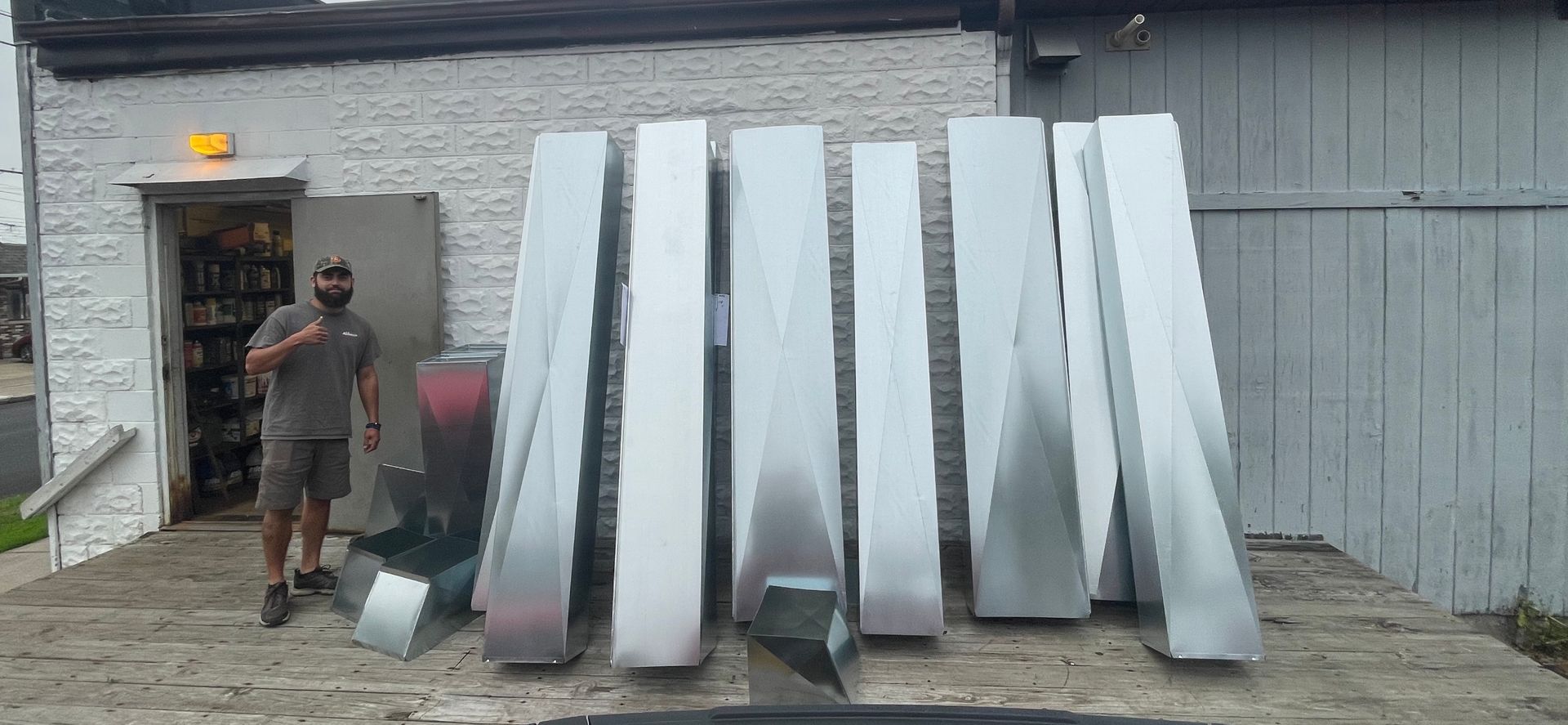 A person stands next to a row of tall, rectangular metal ductwork sections outside a building.