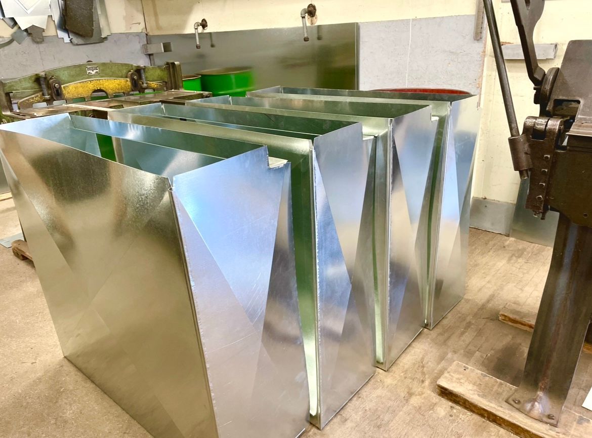 Several rectangular galvanized metal ducts lined up in a workshop setting.