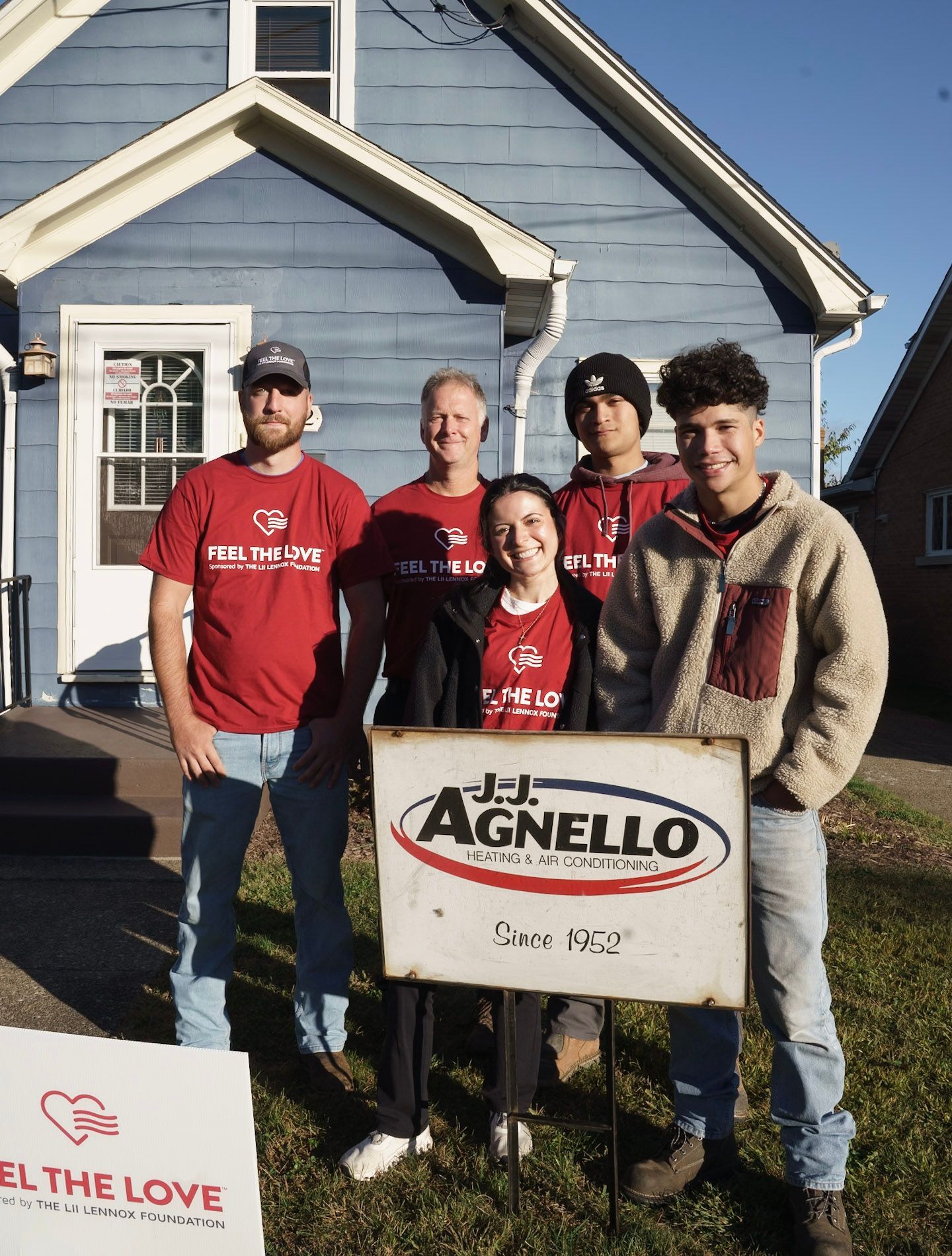 Five people stand in front of a blue house holding a sign for J.J. Agnello Heating & Air Conditioning.