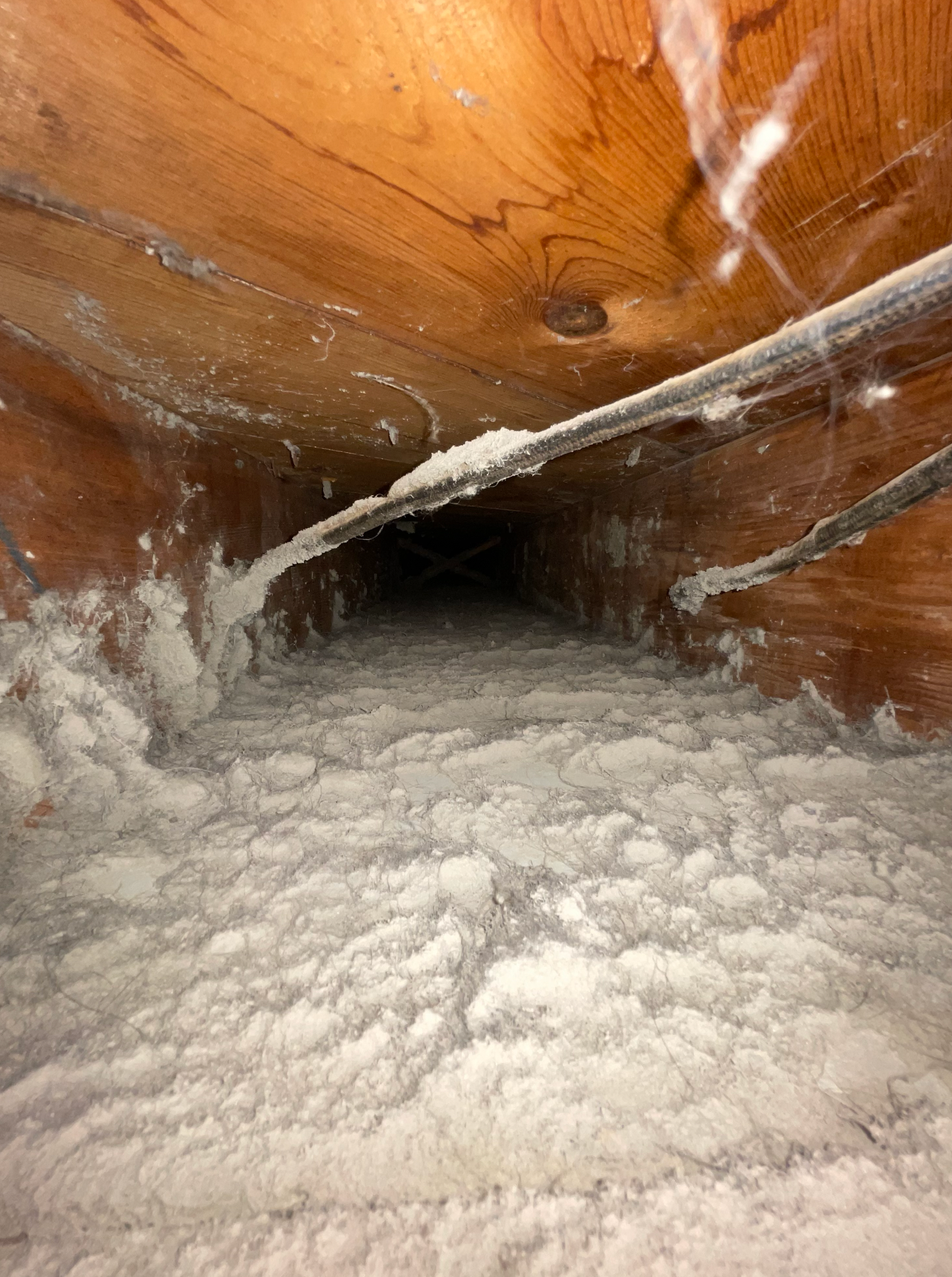 A view inside an attic crawl space featuring white blown-in insulation between wooden joists and electrical wiring.