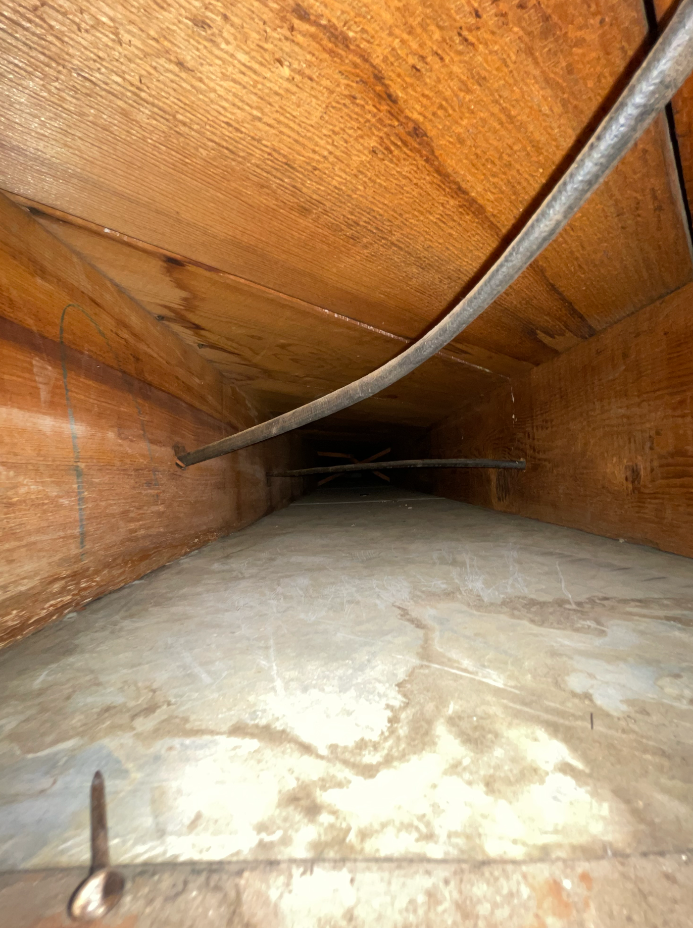 Looking into a wooden joist space with insulation at the bottom, an electrical wire, and a stray nail in the foreground.