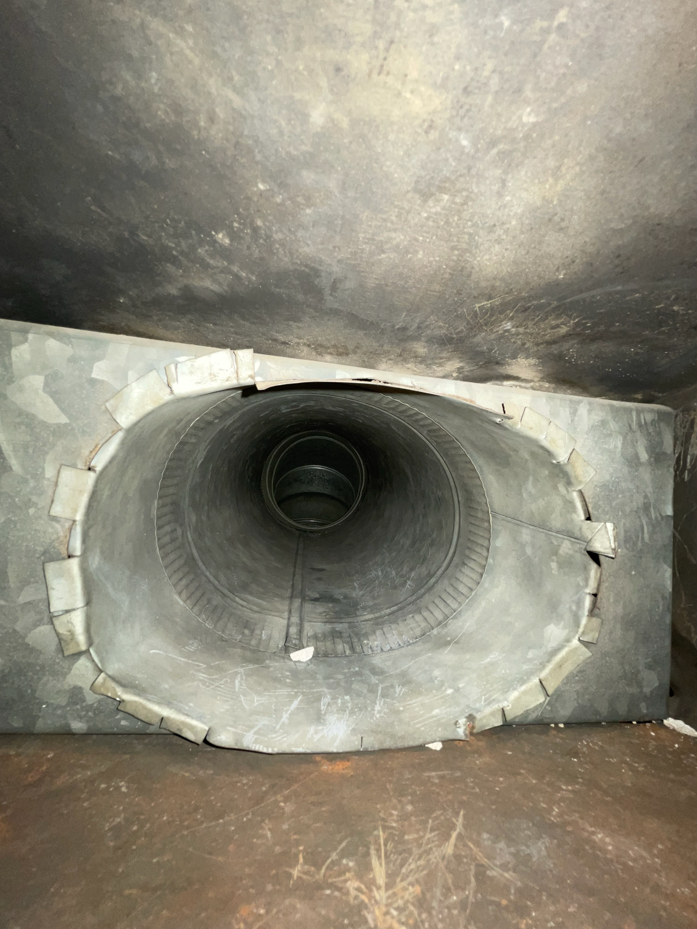 A metallic, circular ventilation duct opening viewed from the front, leading into a dark, recessed tunnel.