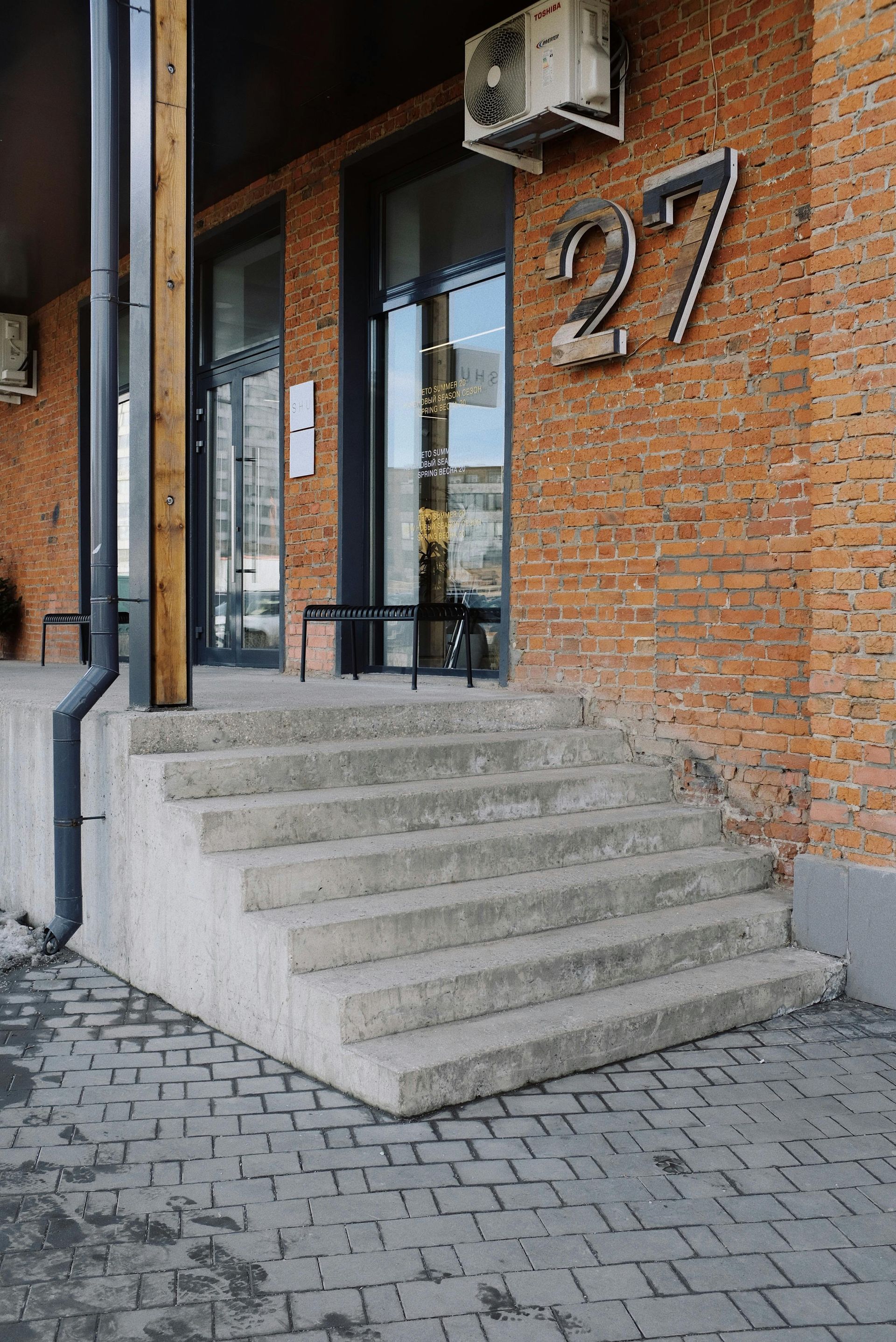 Exterior of a brick building entrance with concrete steps and the number 27.