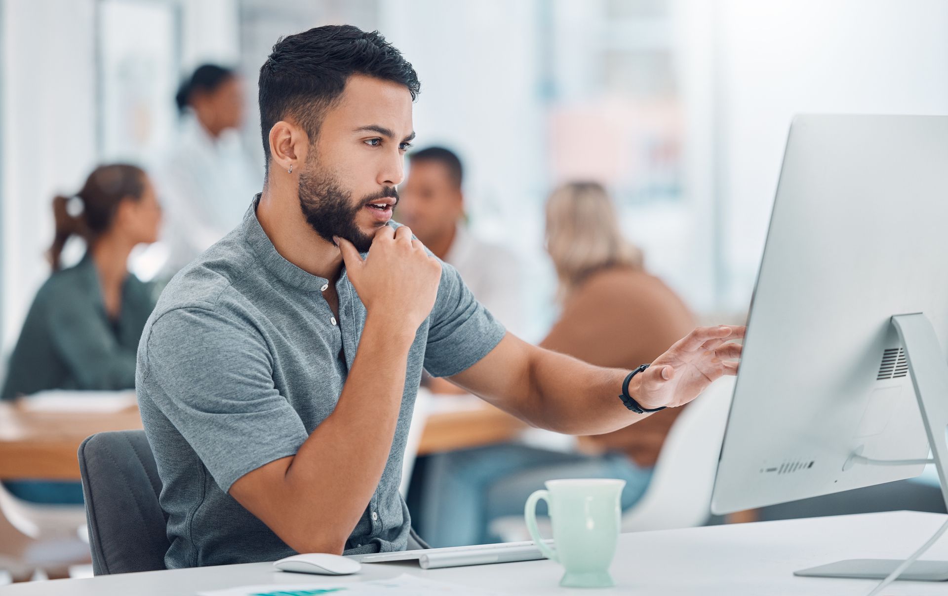 A man is sitting at a desk looking at a computer screen.