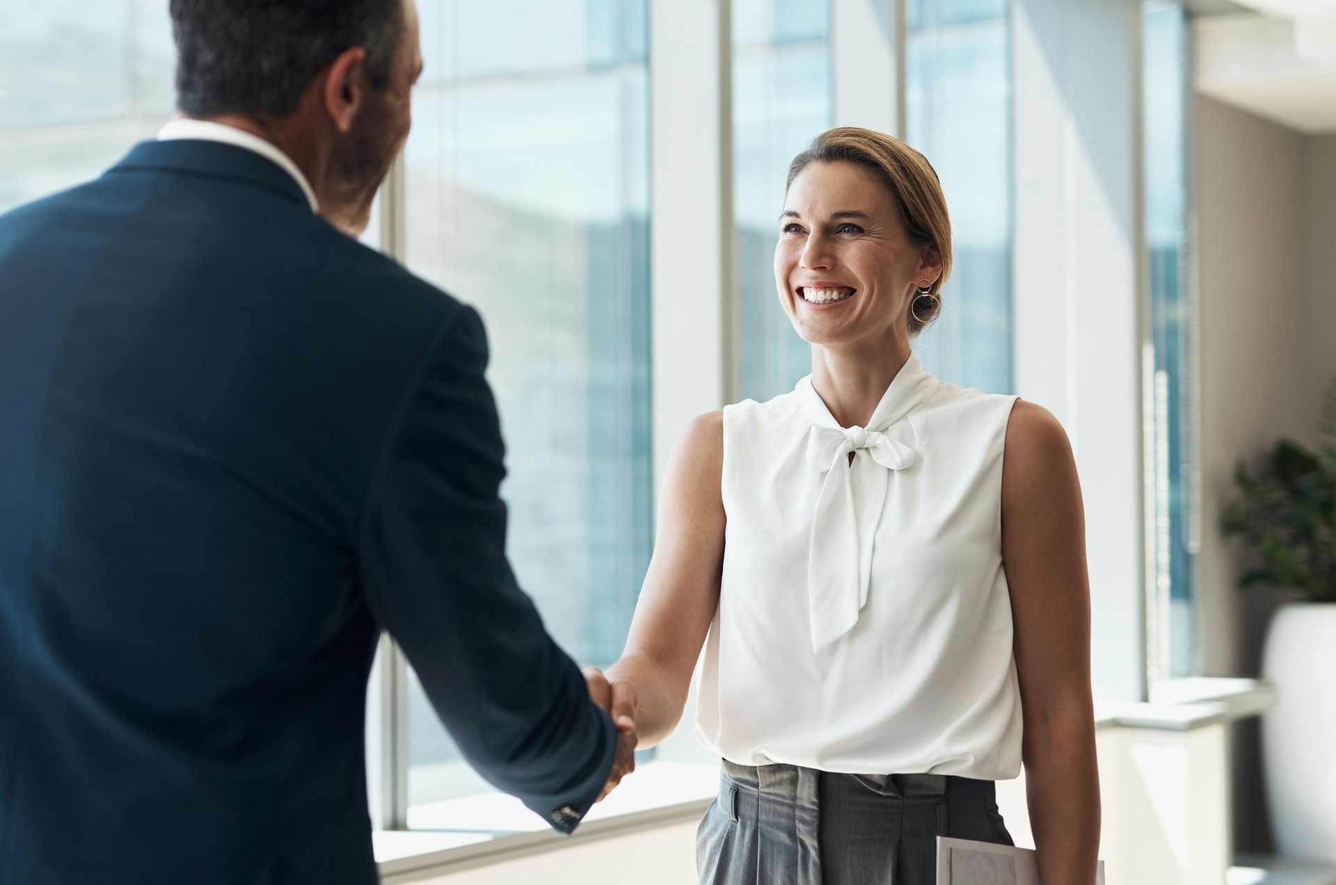 A man and a woman are shaking hands in an office.