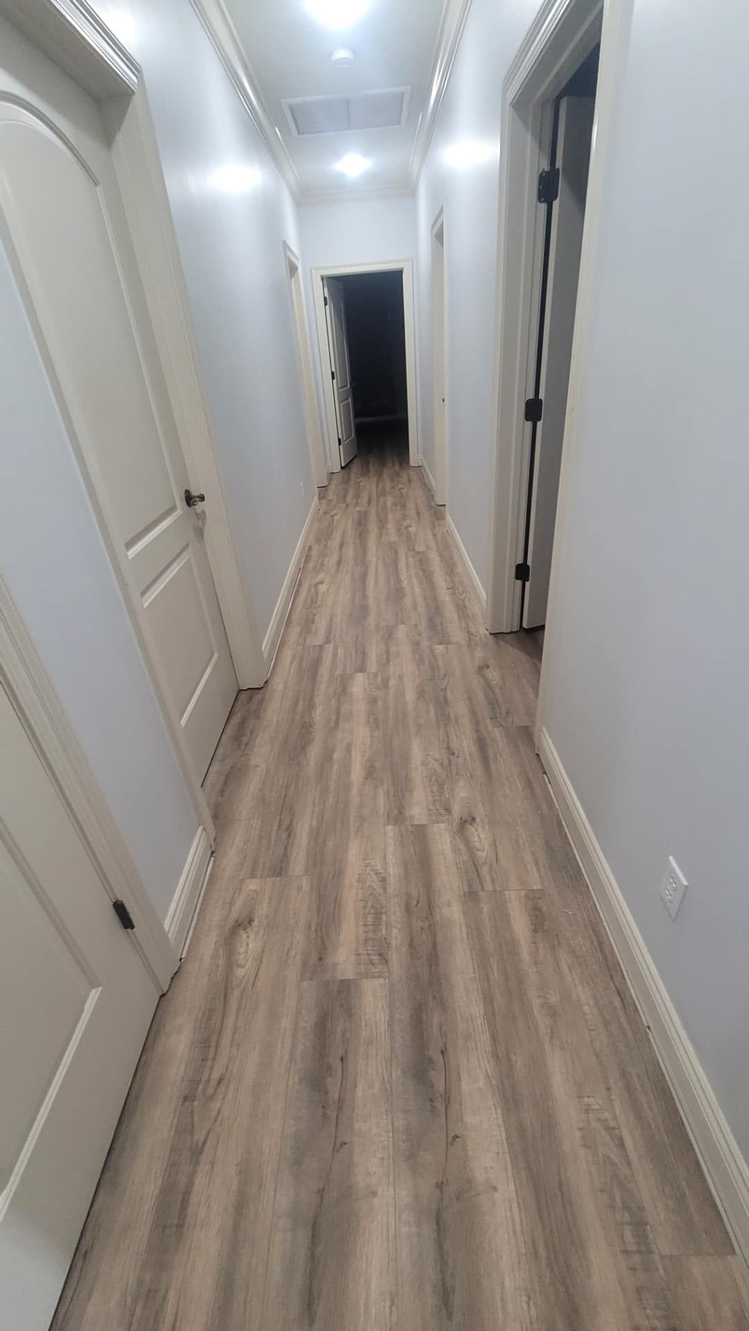 A long hallway with hardwood floors and white doors in a house.