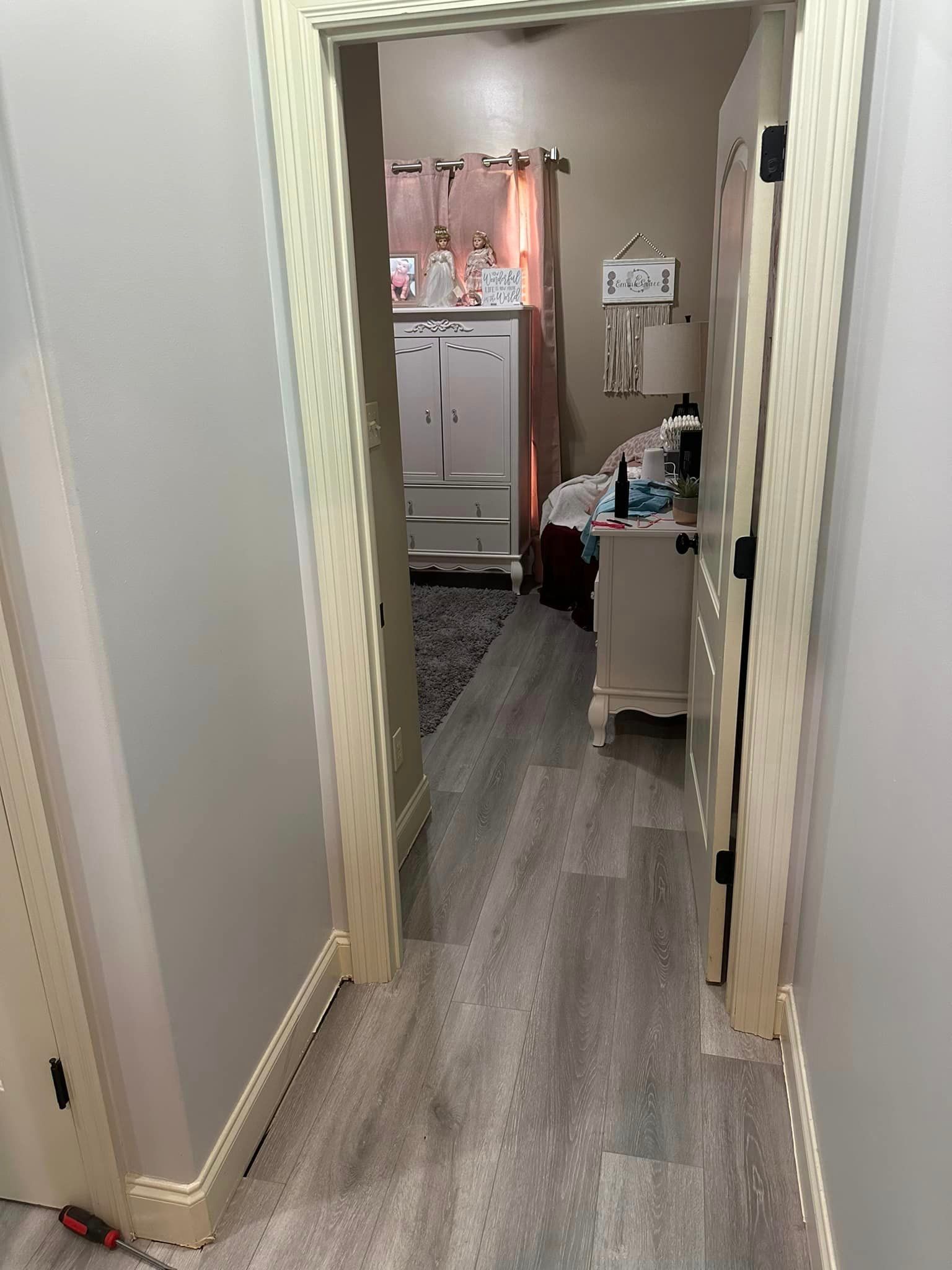 A hallway leading to a bathroom with hardwood floors and a dresser.