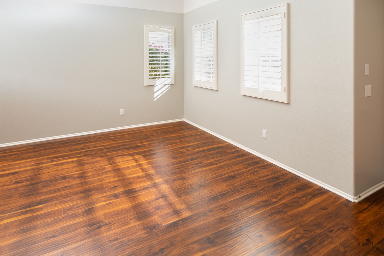 Empty room with wood flooring, light gray walls, and white shuttered windows.