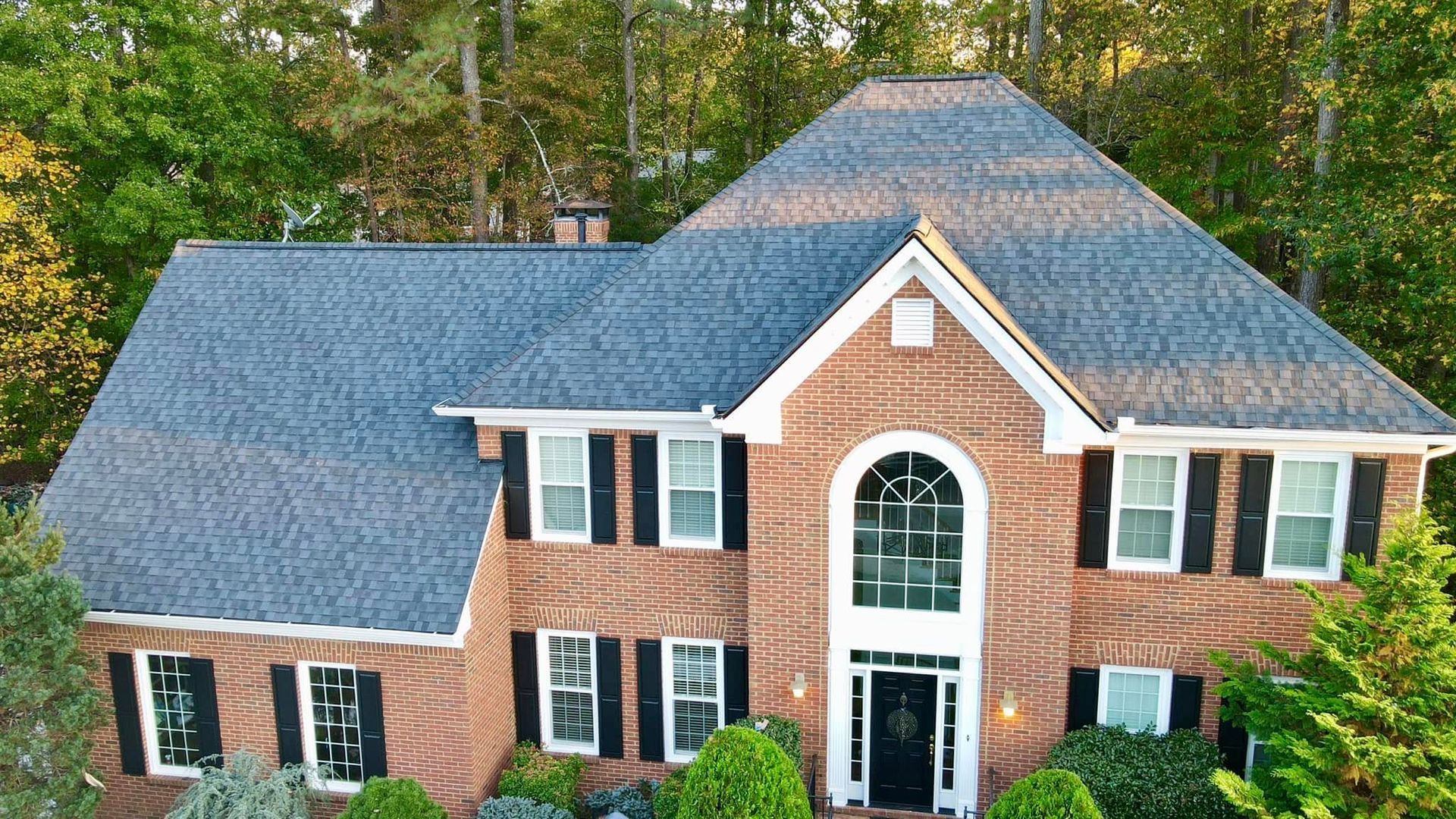 An aerial view of a large brick house with a blue roof surrounded by trees.