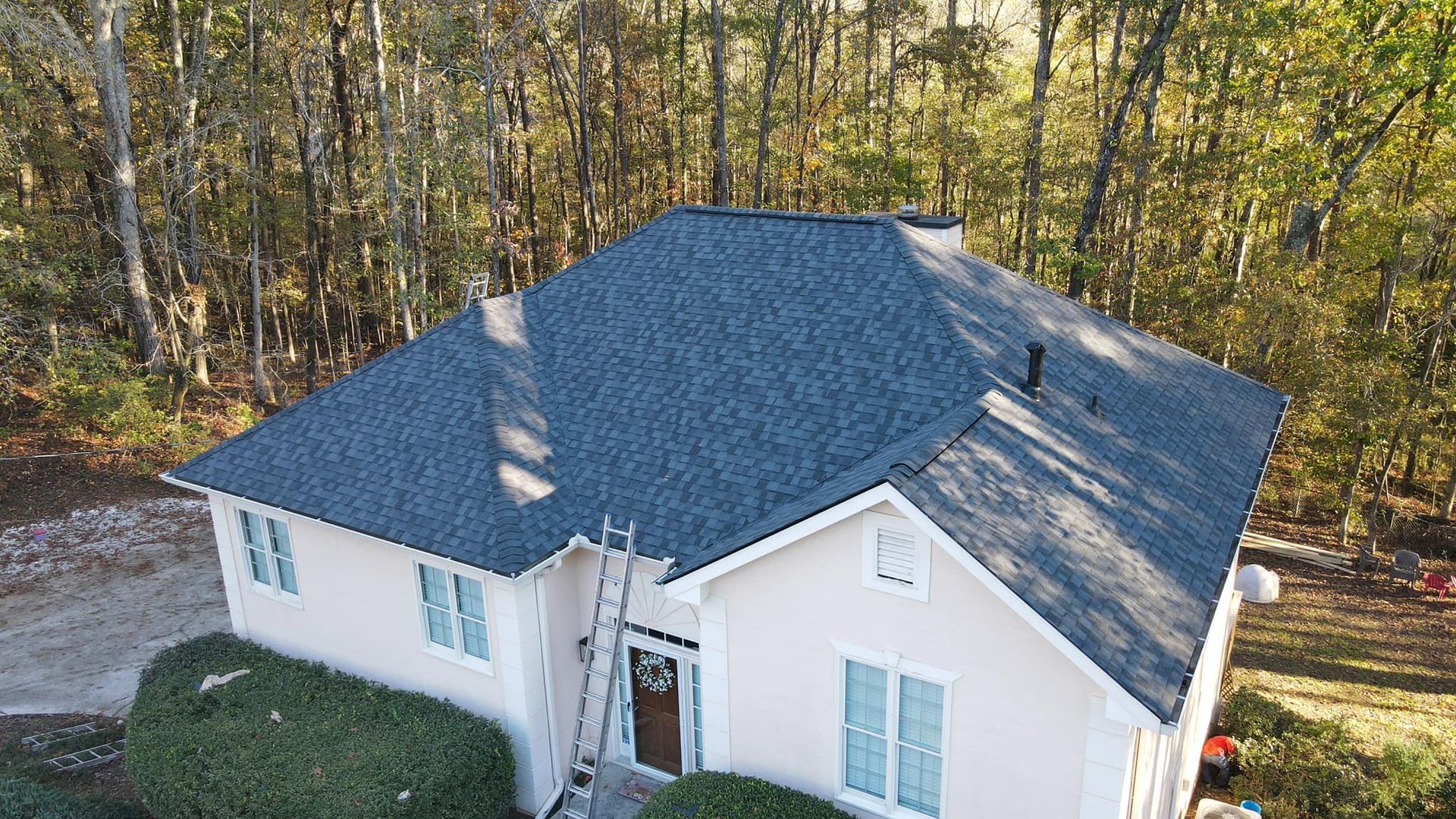 An aerial view of a white house with a blue roof surrounded by trees.