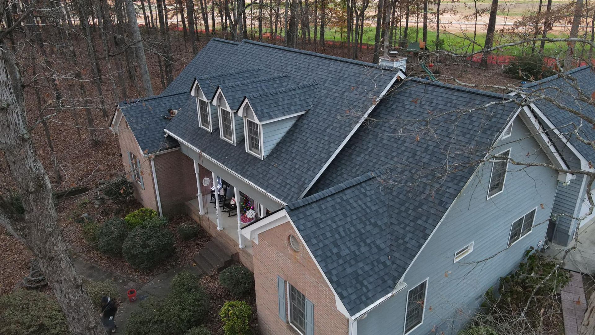 An aerial view of a house with a new roof surrounded by trees.