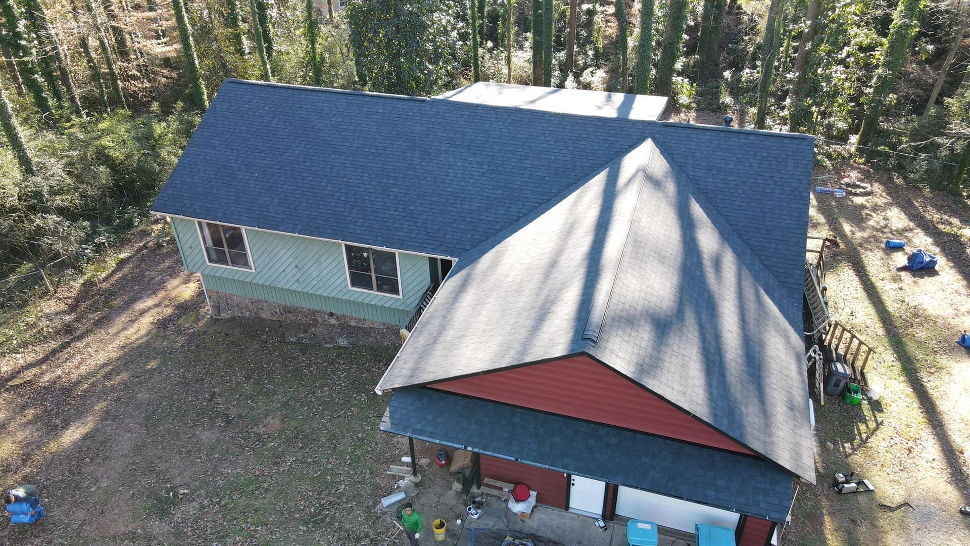 An aerial view of a house with a blue roof in the middle of a forest.