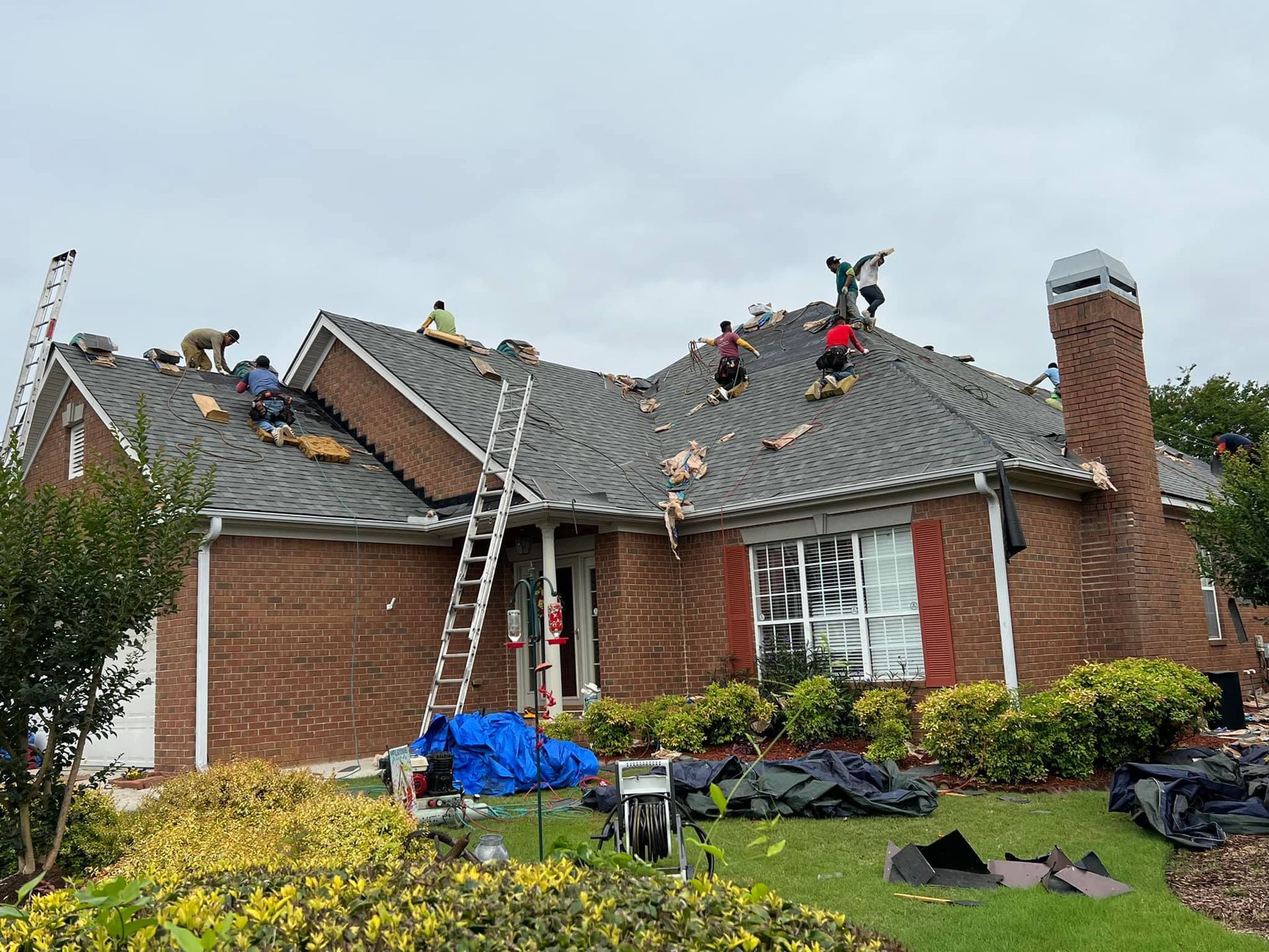 A group of people are working on the roof of a brick house.