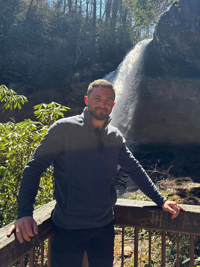 A man is leaning against a railing in front of a waterfall.