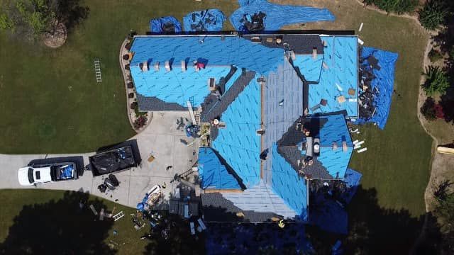 An aerial view of a house under construction with blue tarps on the roof.