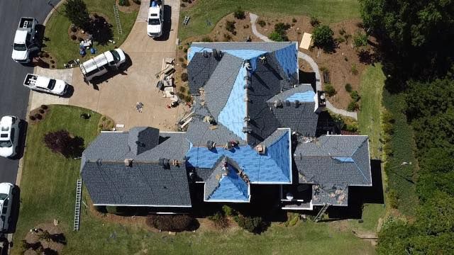 An aerial view of a house under construction with a blue tarp on the roof.