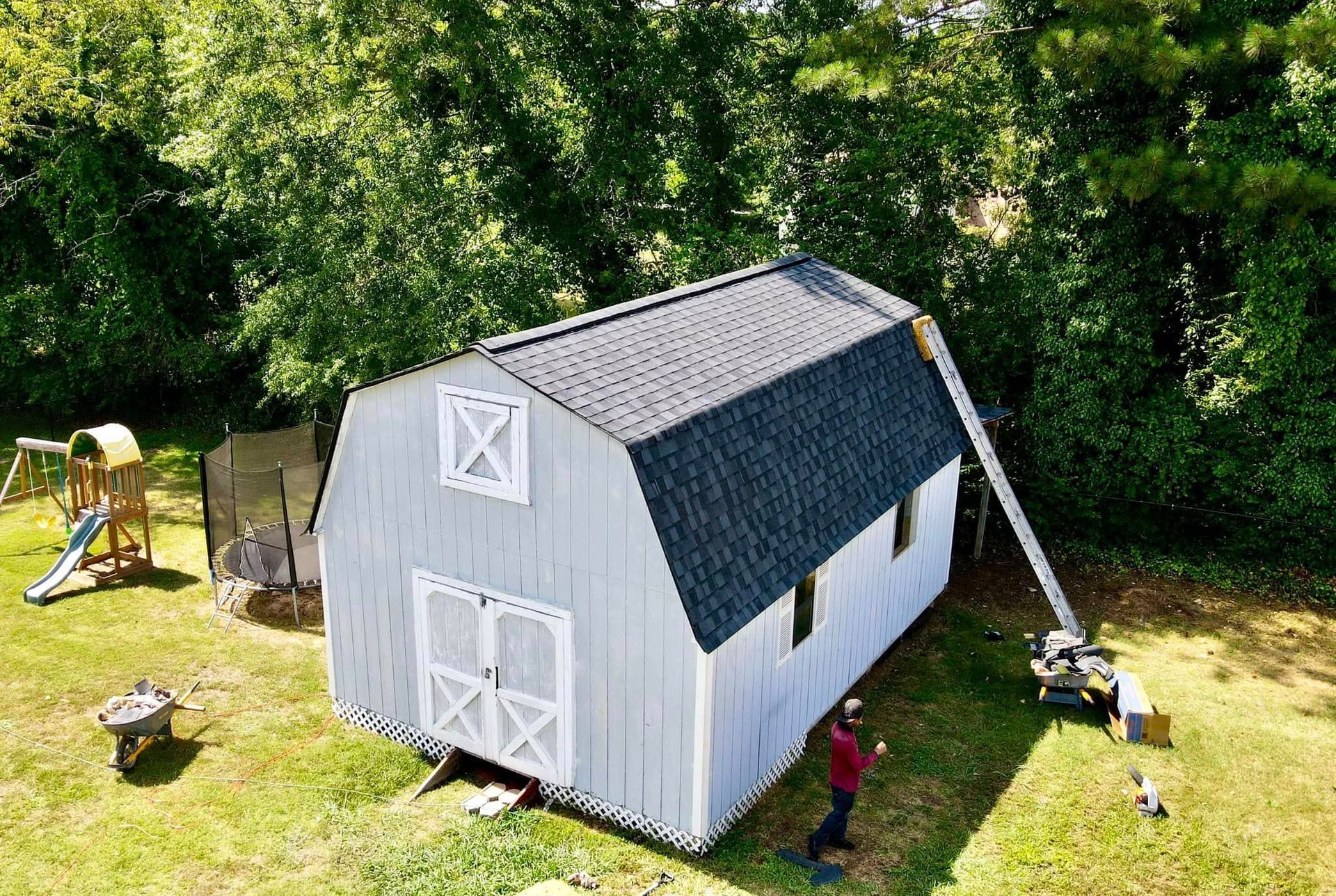 A man is standing in front of a white barn with a black roof.