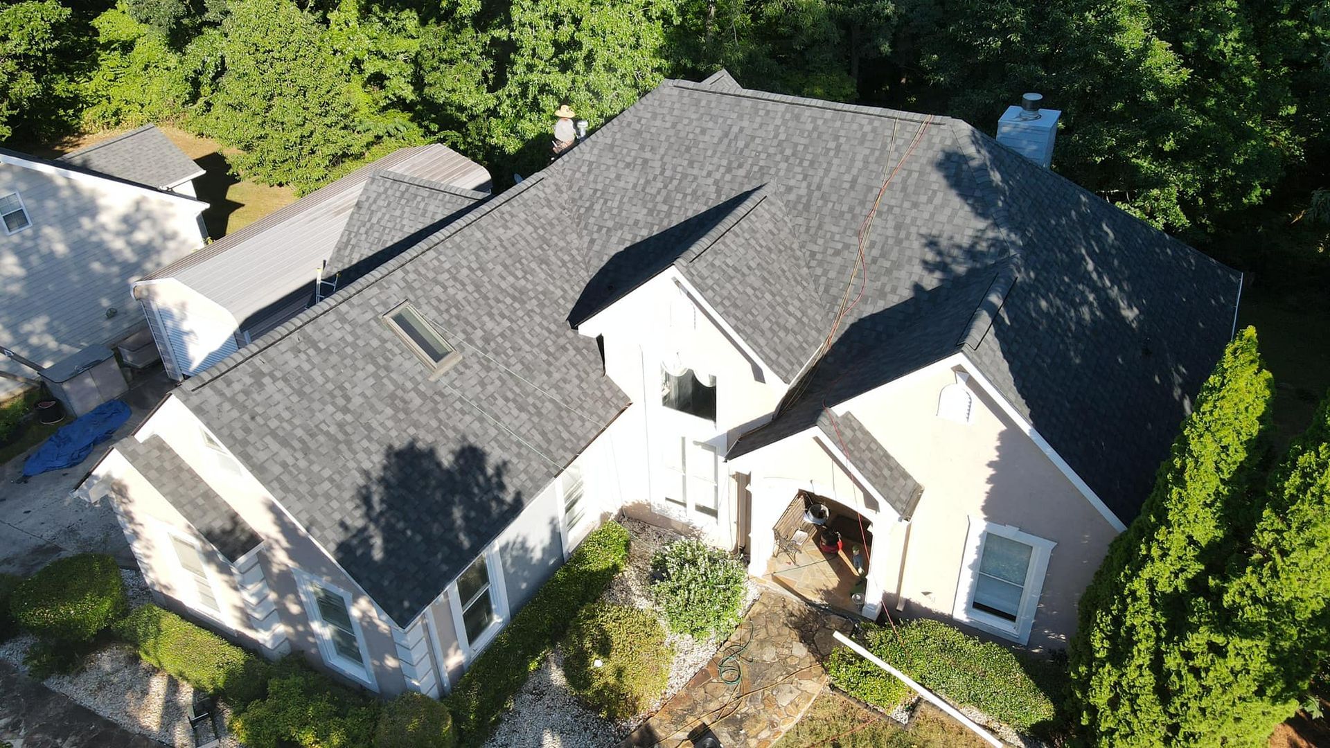 An aerial view of a large house with a gray roof surrounded by trees.