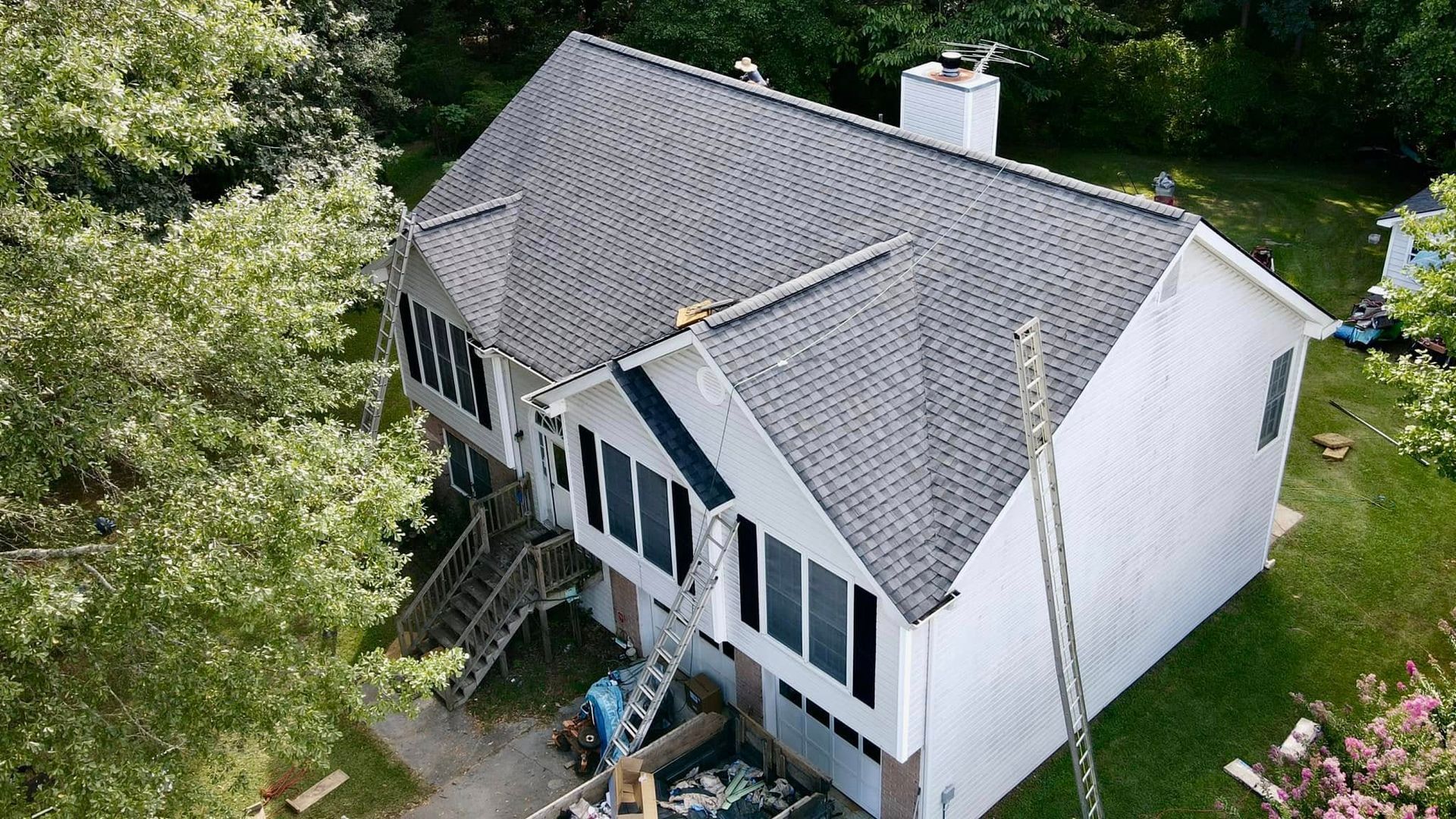 An aerial view of a white house with a gray roof being painted.