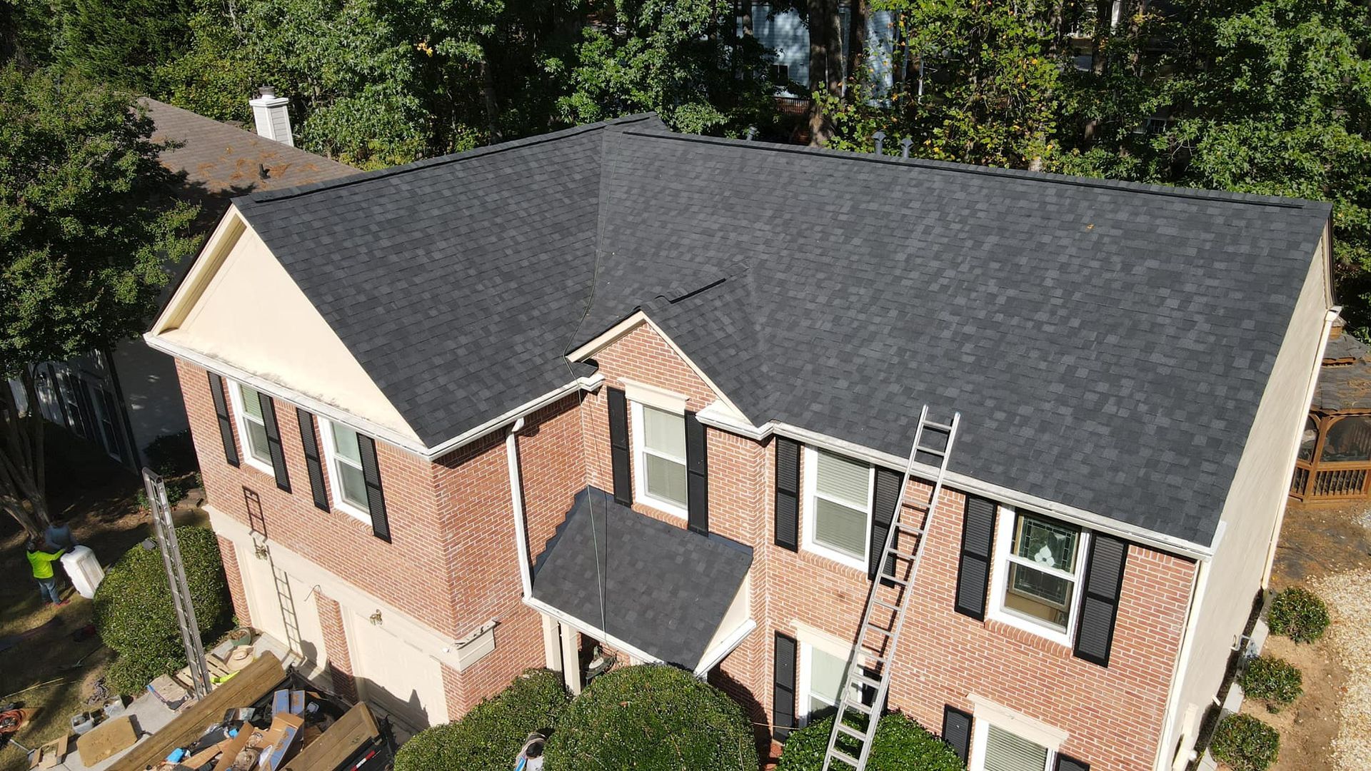 An aerial view of a large brick house with a new black roof.