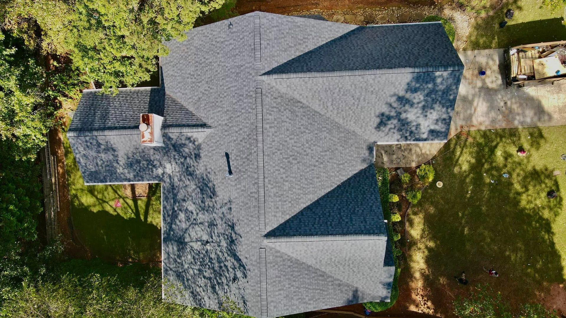 An aerial view of a house with a roof in the middle of a forest.