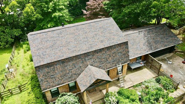 An aerial view of a house with a roof that is surrounded by trees.