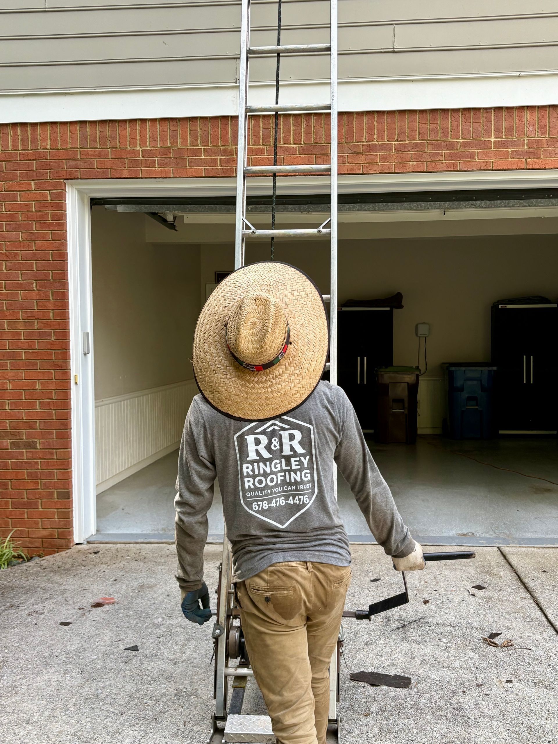 A man wearing a straw hat is walking up a ladder to a garage door.