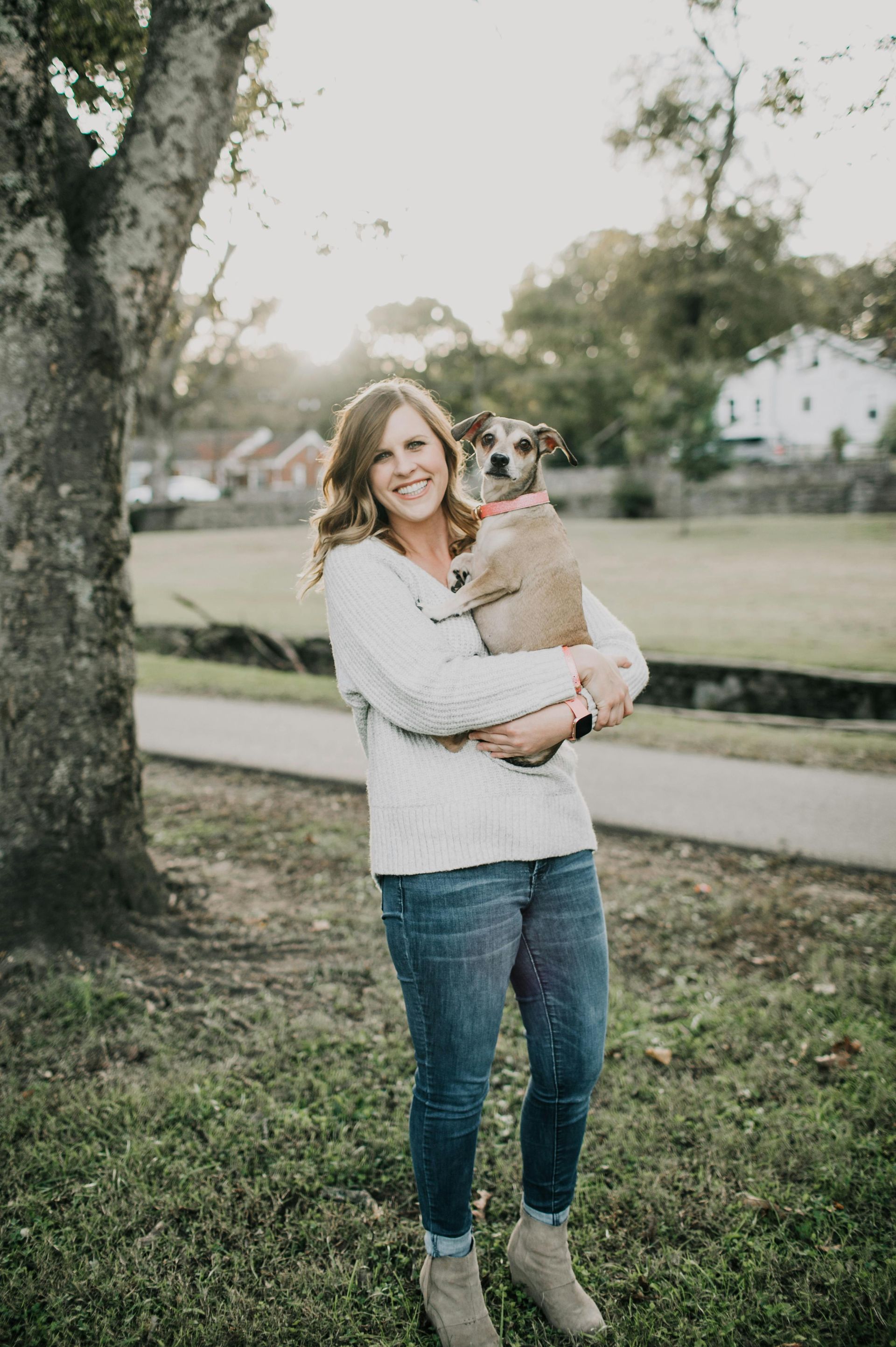 A woman is holding a dog in her arms in a park.