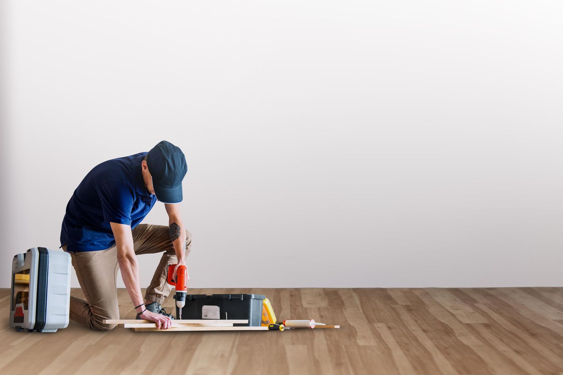 A man is kneeling down on the floor working on a piece of wood.