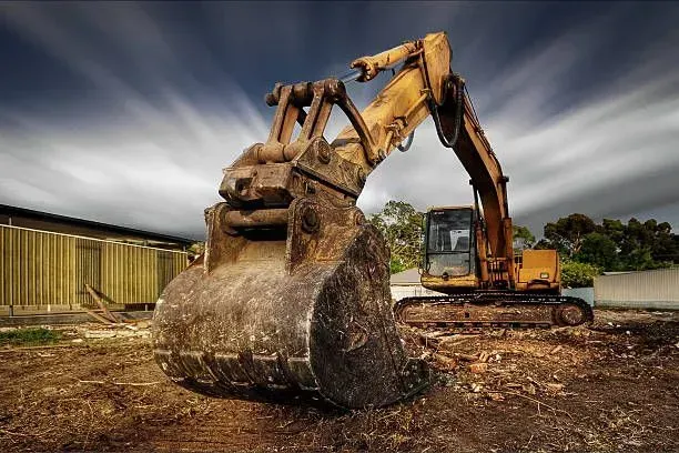 Yellow excavator at a construction site, bucket low, preparing to dig. Overcast sky.