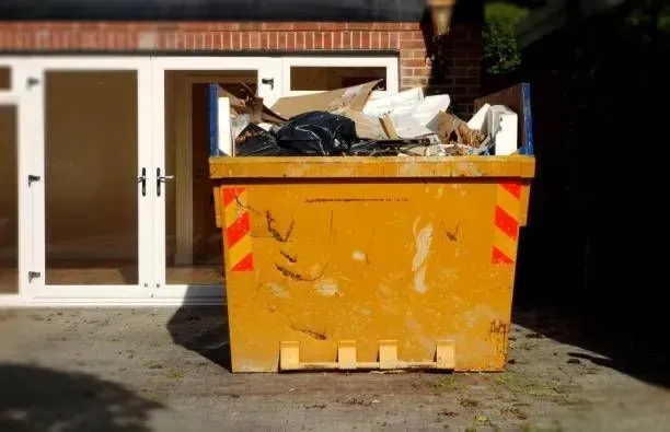 Yellow skip overflowing with debris, set outside a building with white doors.