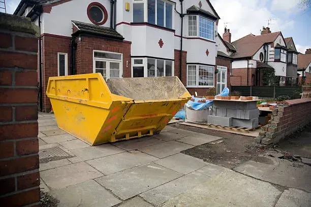 Yellow skip bin on a driveway in front of a house, brick wall on the side.