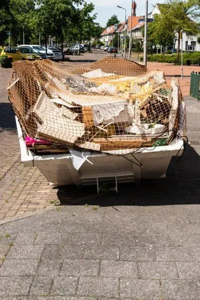 A white dumpster overflowing with debris, covered by a brown net, on a street.