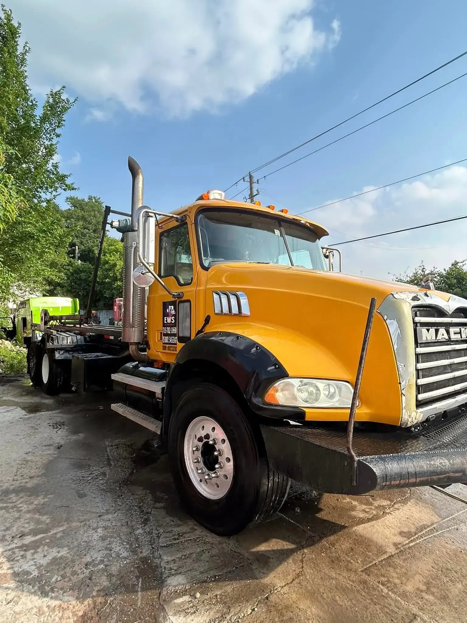 Yellow Mack truck parked under a blue sky, with black fenders and silver wheels.