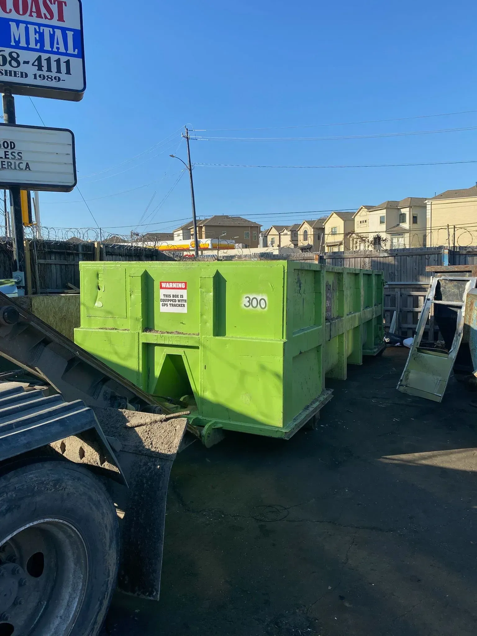 Green dumpsters lined up outdoors near a sign for Coast Metal on a sunny day.