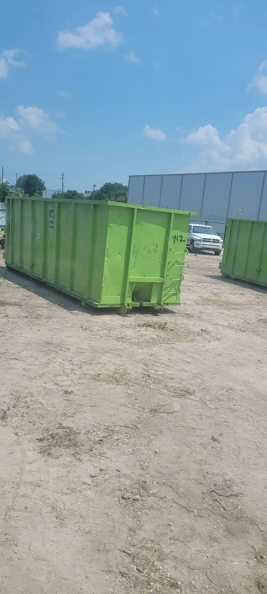 Green dumpsters on dirt under a bright blue sky with white clouds.