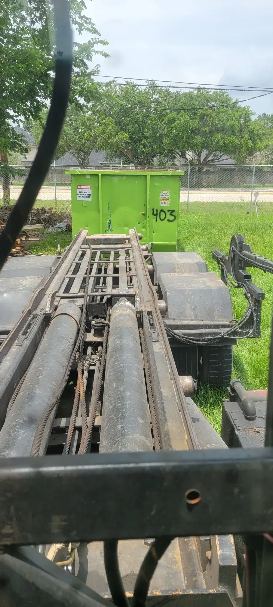 A green dumpster on a trailer. The shot is from the driver's perspective. Trees and grass are in the background.