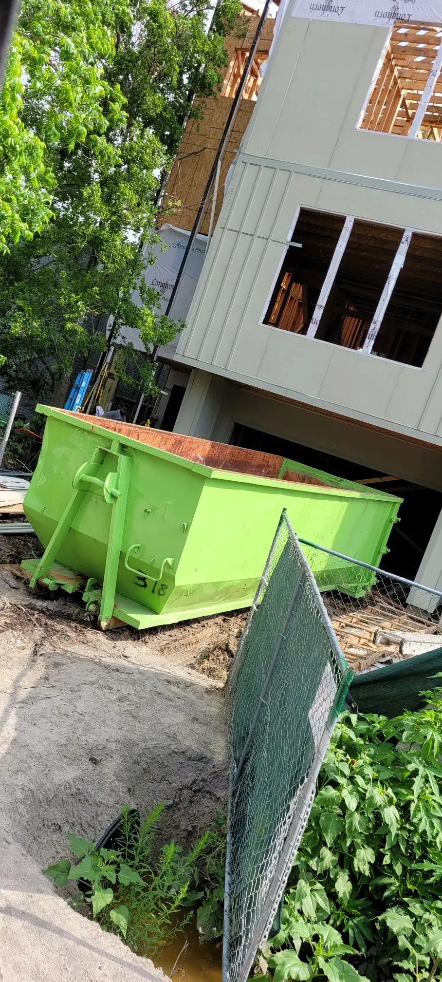 Green dumpster filled with debris next to a building under construction.